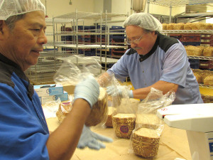 Frank along with Miguel assist in slicing bread for TABLE using the funds from a previous fund-raising campaign.
