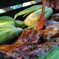 hand brushing barbecue sauce onto meat on grill