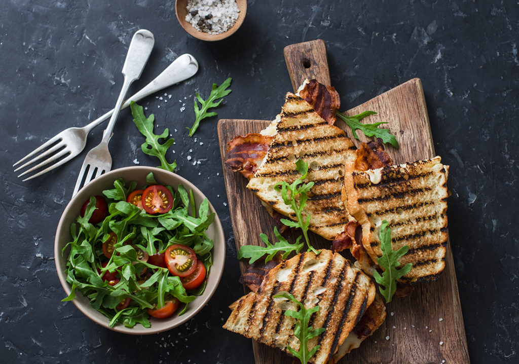 Grilled bacon sandwiches on wooden cutting boards and arugula, cherry tomato salad