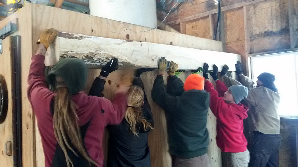people lifting a beam into place in the sugar shack