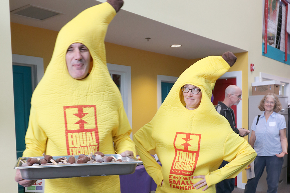 Two people in banana costumes hold a tray of chocolate bananas to eat