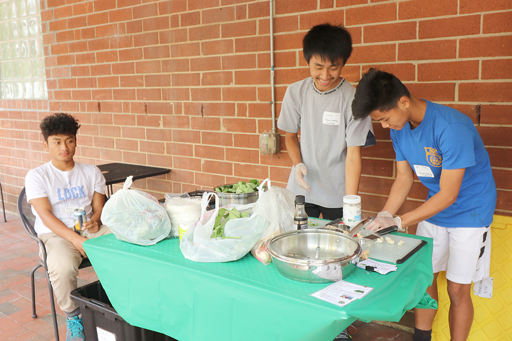 Three teenage boys cutting and cooking spinach