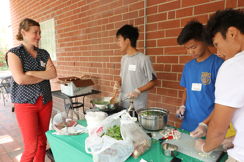 Kelly watches three teenage boys chopping and cooking water spinach at an outdoor table