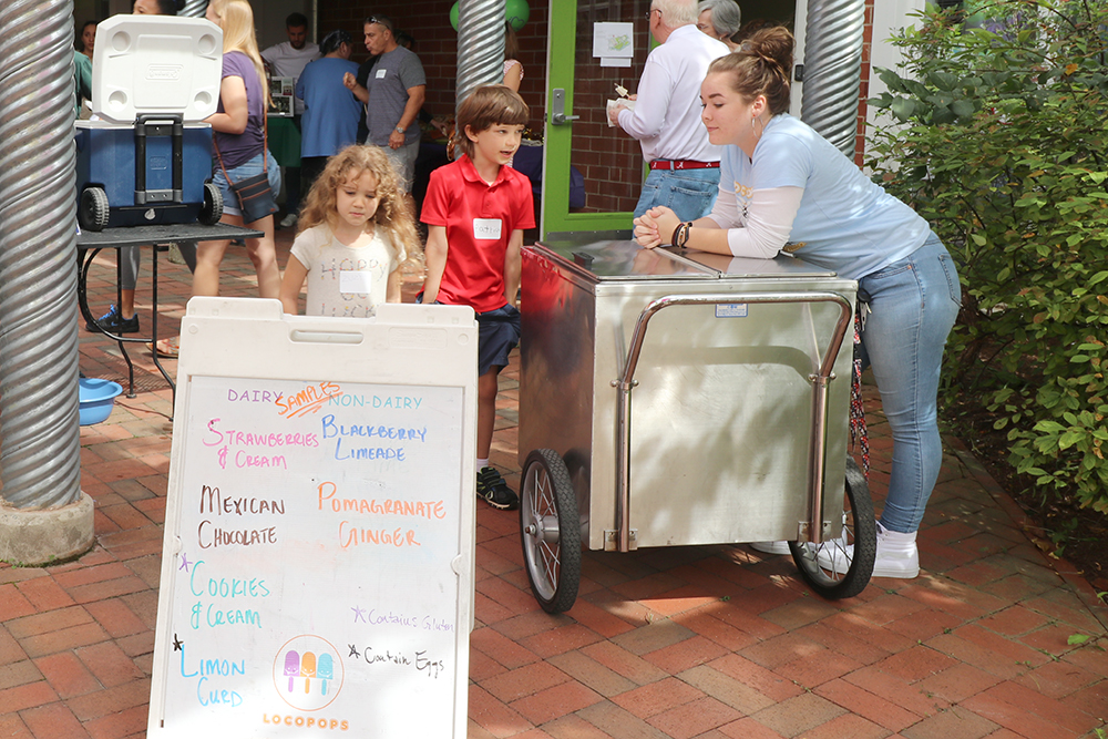 woman leaning on ice cream cooler, talking to kids, with a Locopops sign