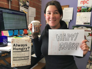 Carolyn holding a happy new year sign and almonds, with her book