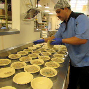 Leo putting pie shells on top of row of pot pies