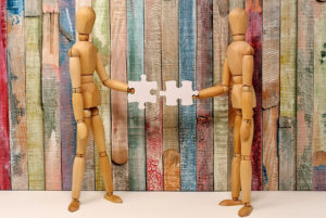 two wooden human figures holding puzzle pieces toward each other