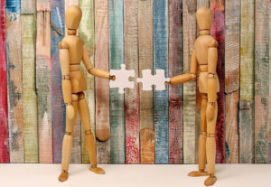 wooden figures holding puzzle pieces that are about to connect