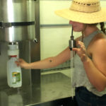 woman in hat holding milk bottle under machine spout