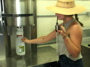 woman in hat holding milk bottle under machine spout