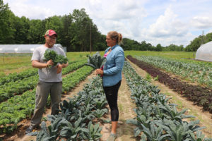 Keith and Megan holding kale bunches in a kale field