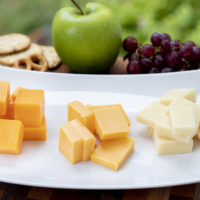 three colors of cheddar cheese on a white dish with apples and grapes