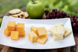 three colors of cheddar cheese on a white dish with apples and grapes