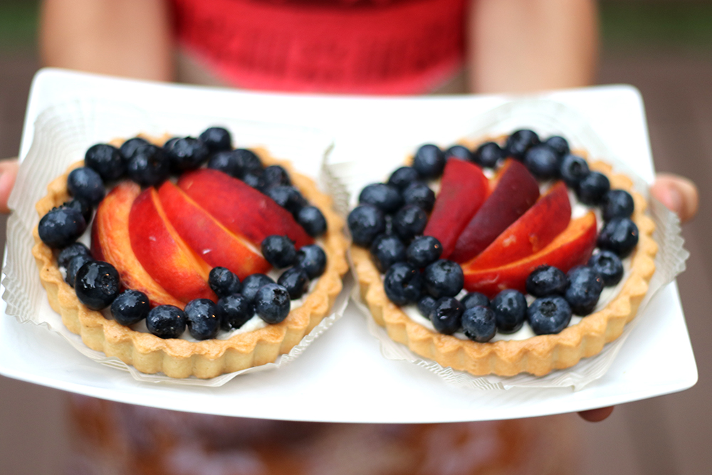small peach blueberry tarts on plate held by hands