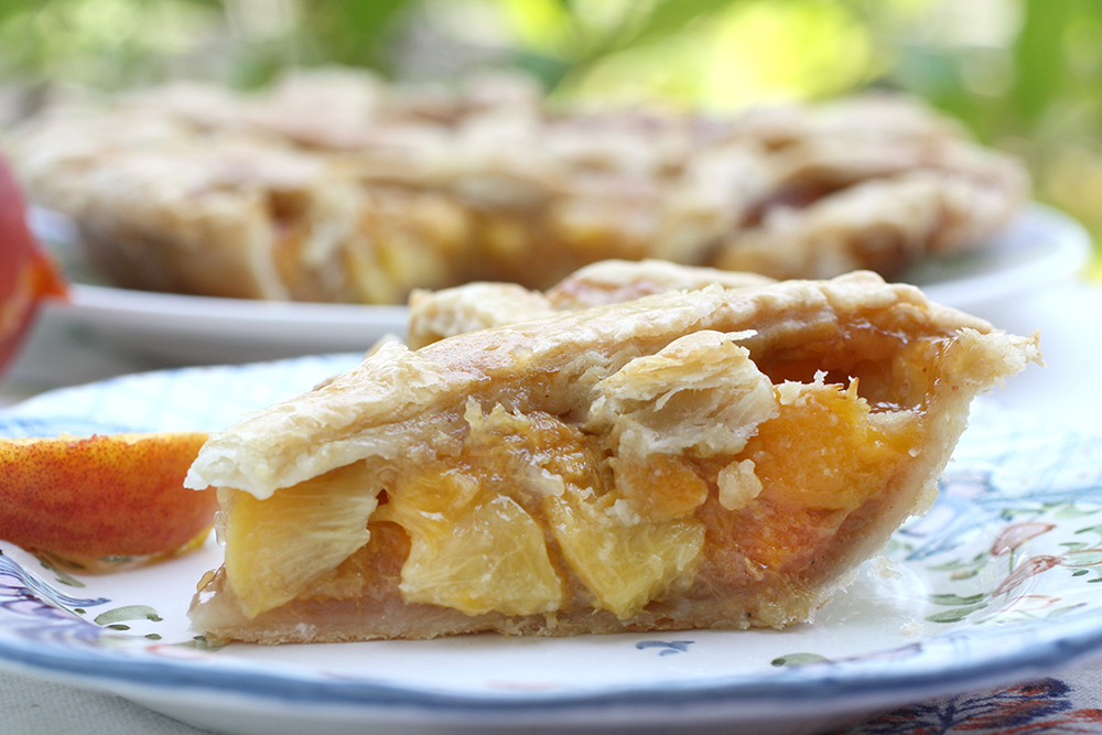 slice of peach pie outdoors on plate with whole pie in back