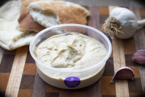 a tub of hummus with pita bread and garlic cloves