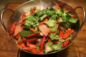 a wok with stir fry in it, containing red hot peppers and cilantro and meat
