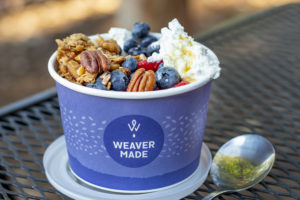 a paper cup filled with nuts, berries, and whipped cream