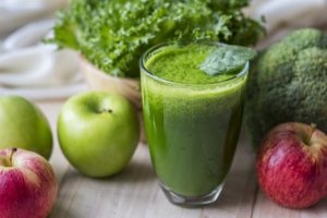 green smoothie in glass with kale and apples around it