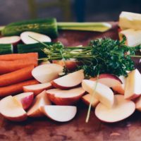 carrots, cucumber, greens, and sliced apples on a cutting board