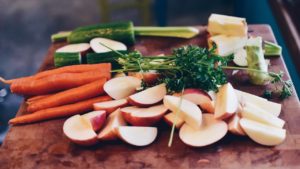 carrots, cucumber, greens, and sliced apples on a cutting board