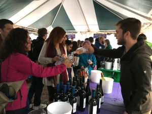 person pouring wine to other person with crowd under tent