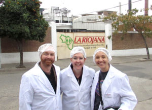 three people in hairnets and lab coats in front of a sign for La Riojana