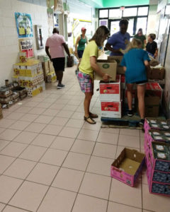 people sort food in boxes and on pallets in school foyer