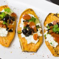 slices of sweet potato topped with cheese, olives, tomato, and cilantro