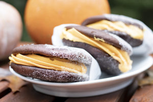 Three whoopie pies with chocolate cookies and orange frosting, on a plate