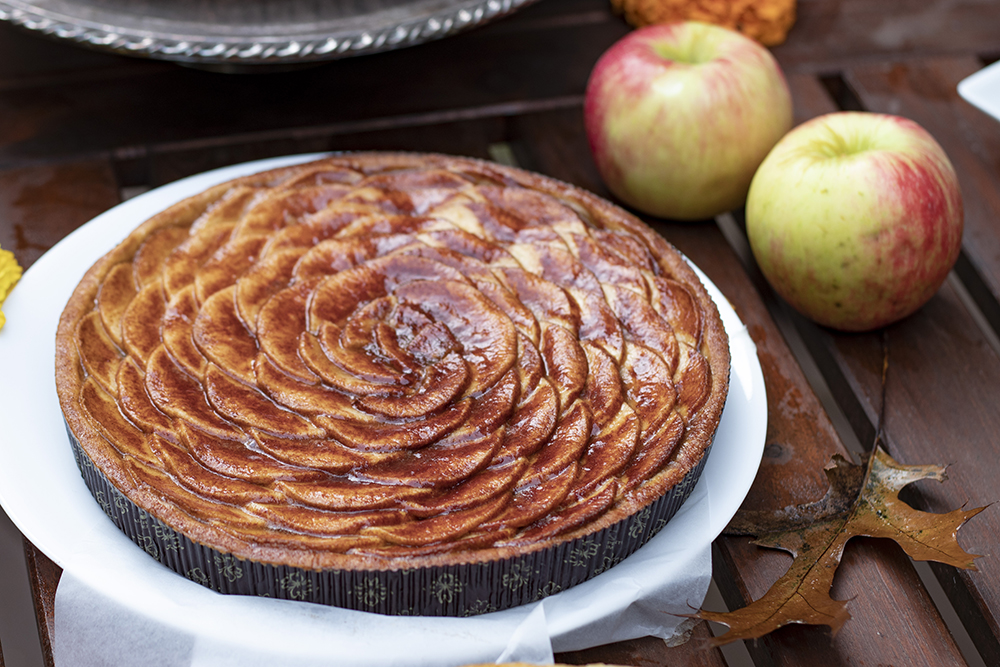 tart with slices of apple layered on top, with apples on table