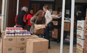 volunteers unloading boxes from pallets of food outside a school