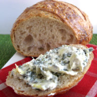 spinach artichoke dip on a slice of sourdough bread with a loaf