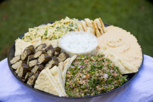 a large platter with tabouli, pita wedges, hummus, tzatziki, pasta salad, and dolmas