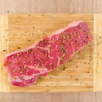 piece of raw beef on a wooden board, with seasoning sprinkled on top