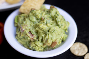 a bowl of guacamole with a chip in it