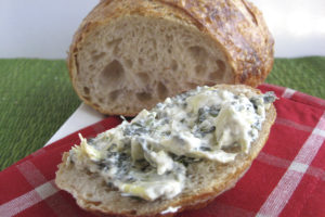 a load of sourdough bread with a slice cut, and the slice is spread with spinach artichoke dip