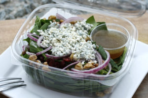 spinach salad with blue cheese crumbles, slices of red onions, walnuts, and dried cranberries on top