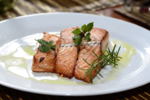 cooked salmon on a plate with herbs and olive oil