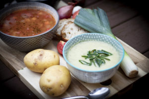 bowls of soup on cutting board with potatoes, leeks, tomatoes, and bread
