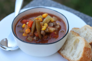 bowl of vegetable beef soup with bread and spoon