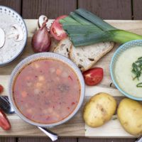 bowls of soup on cutting board with potatoes, leeks, mushroom slices, tomatoes, and bread