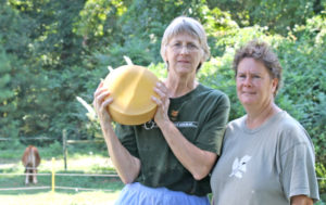 Portia and Flo holding a wheel of cheese outside