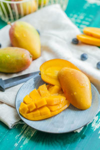 a cut mango on a plate, with whole mangos in back