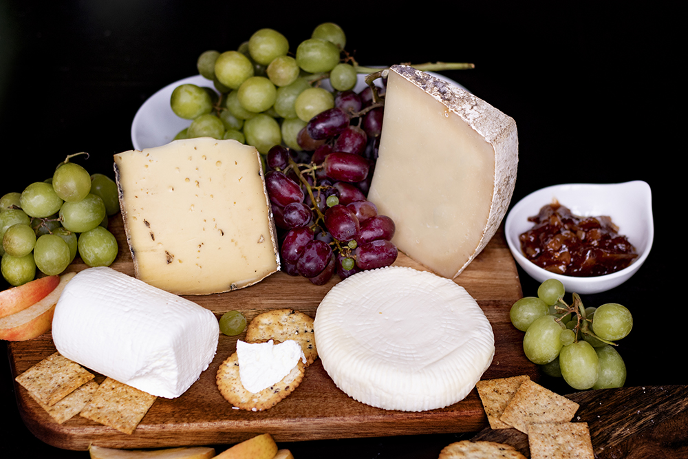 cutting board with several cheeses and grapes