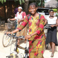 women in African print clothing pushing bicycles and smiling