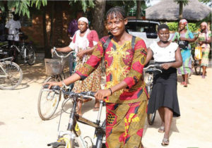 women in African print clothing pushing bicycles and smiling
