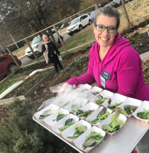 woman in community garden holding tray with samples of green leafy vegetable for eating