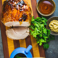 glazed ham with slices cut, on cutting board, with bowl of mustard, bunch of parsley, and other bowls