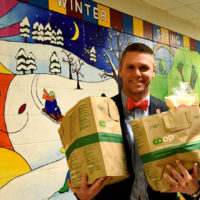 man holding two bags of groceries in a elementary school hallway with paintings on the walls